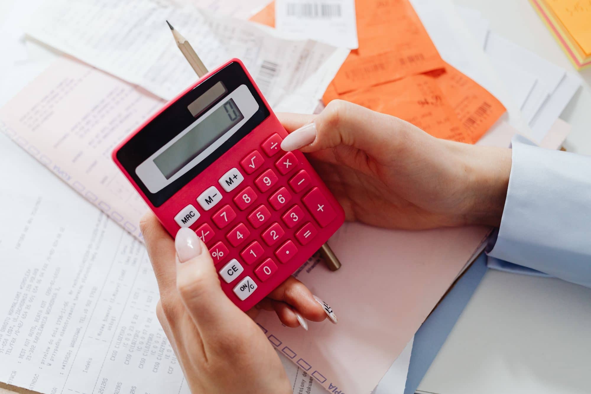 Hands holding a pink calculator above receipts and a pencil