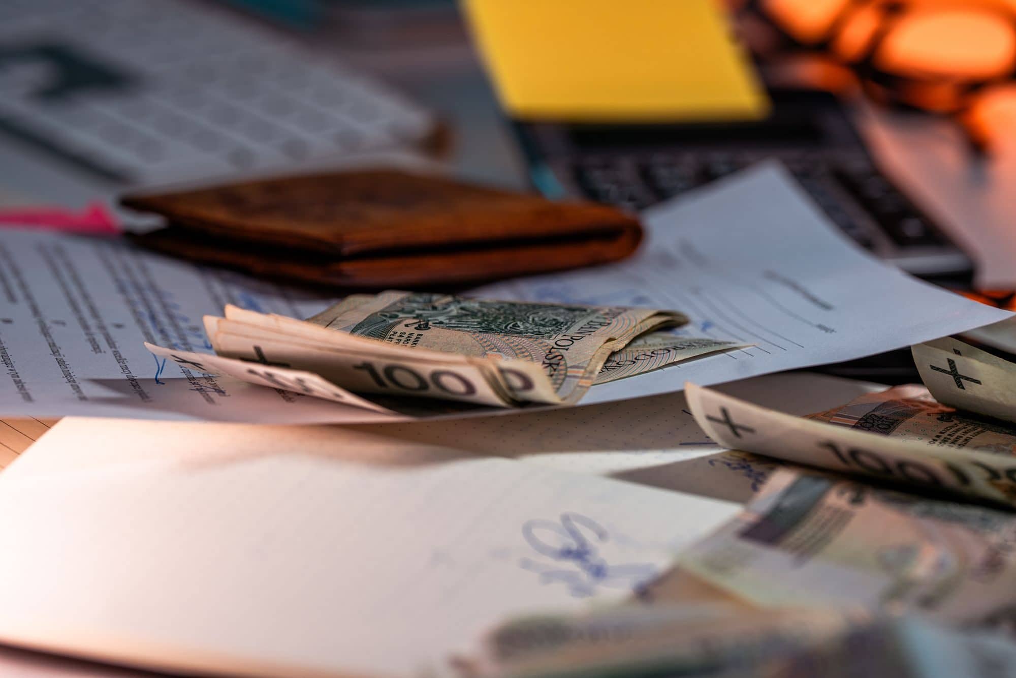 Paper money and a leather wallet on a desk covered in financial documents