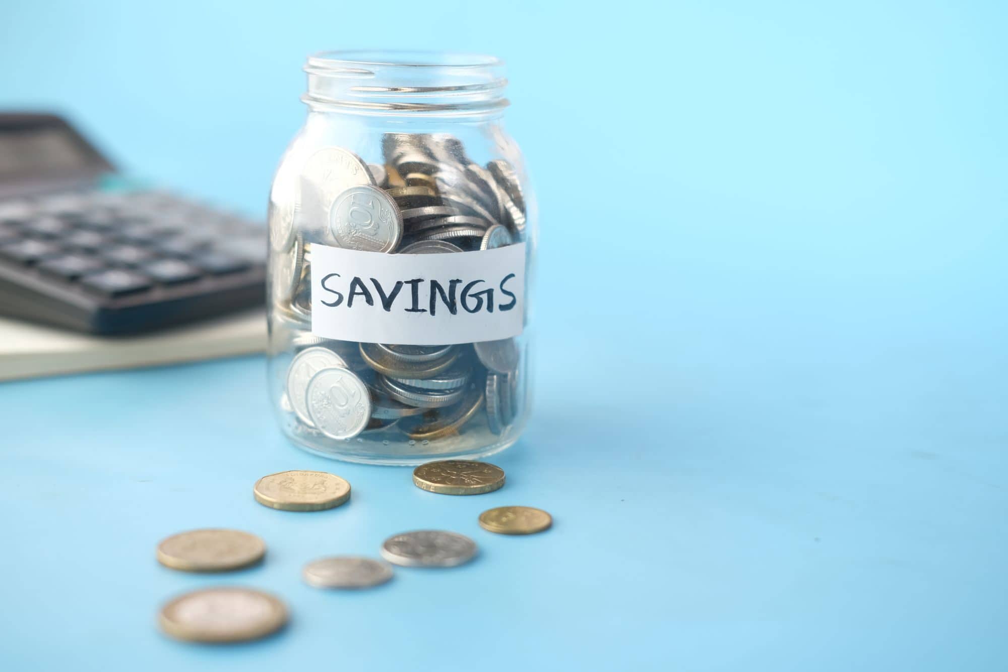 A glass jar of coins labeled Savings next to a calculator