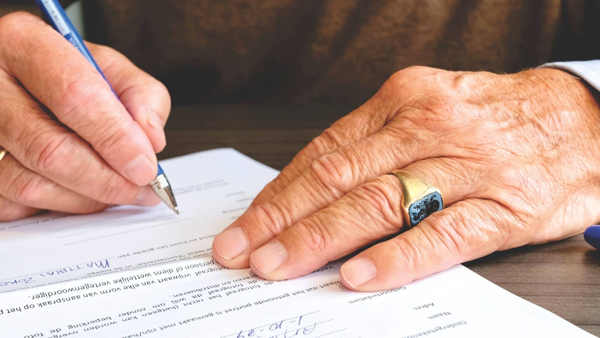 An older person's hands sign a document with a ballpoint pen