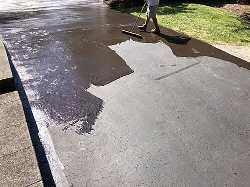 Sealcoat being squeegeed onto a gray asphalt driveway, half of it already coated black