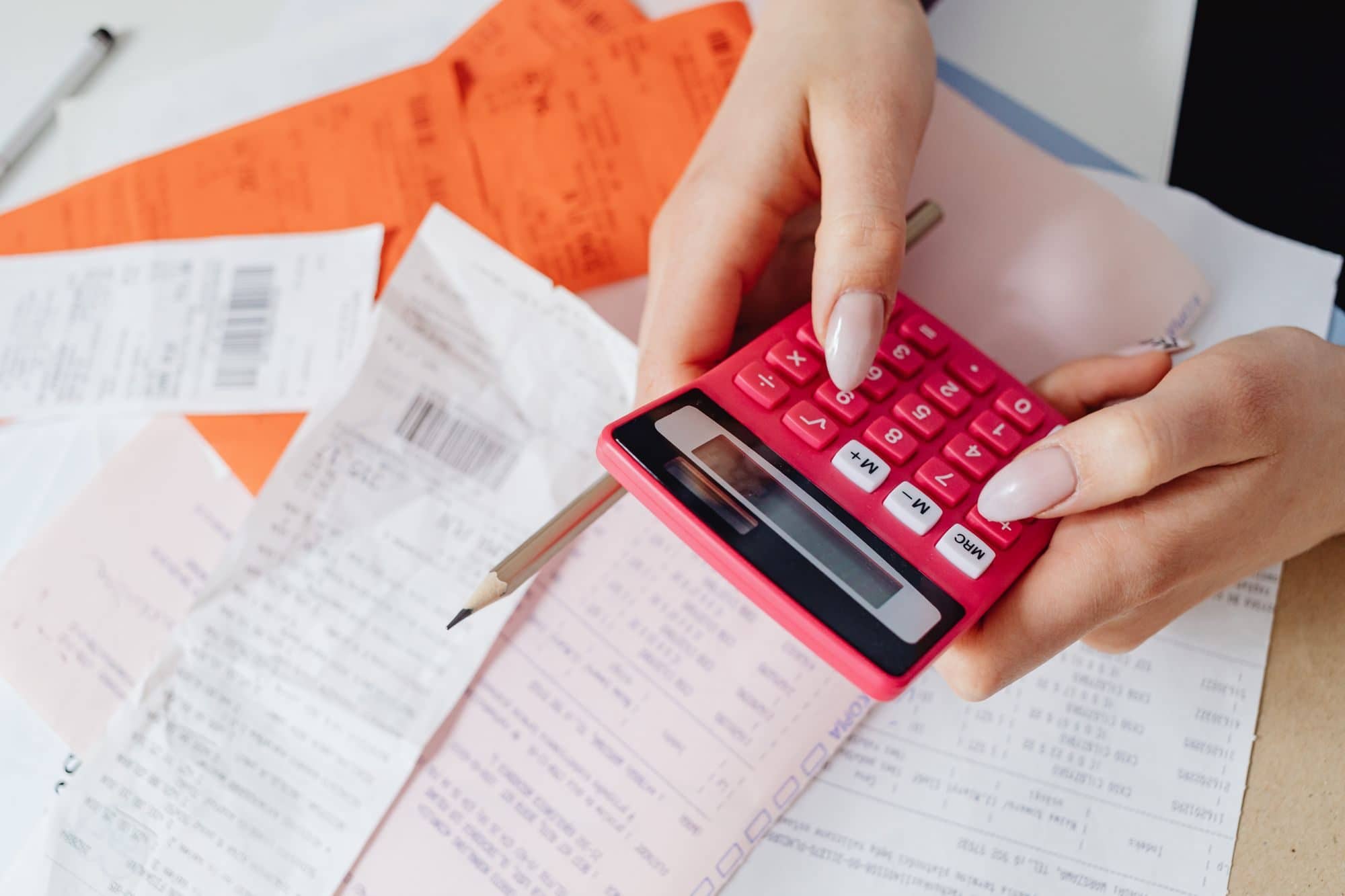 Hands using a pink calculator over a pile of paper receipts and bills